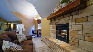 A cozy living room with a stone fireplace, a brown leather sofa, and a dining area in the background. - Branson White River Suite: A Private Forest Retreat (Reeds Spring)