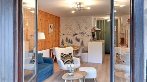 A modern living room with a wooden wall, a blue sofa, a white armchair, and a dining area in the background.