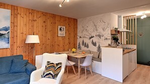 A compact living space with a wooden wall, a dining area, a kitchenette, and a sofa.