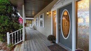 A covered porch with a wooden railing, a welcome mat, and a door with a stained glass window. - Mountain Meadows Retreat - A Romantic Escape Overlooking the Ozark Mountains (Reeds Spring)