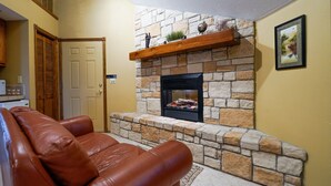 A living room with a stone fireplace, a brown leather couch, and a wooden shelf above the fireplace. - The Expedition: Our Flagship Suite (Reeds Spring)