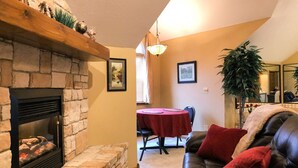 A living room with a fireplace, a dining area with a red tablecloth, and a leather couch with red cushions. - The Expedition: Our Flagship Suite (Reeds Spring)