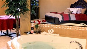 A hotel room with a large bathtub, a bed with a red and gray blanket, and a potted plant. - The Expedition: Our Flagship Suite (Reeds Spring)