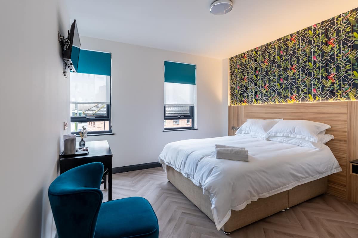 A modern hotel room with a bed, a desk, a chair, and a large window.