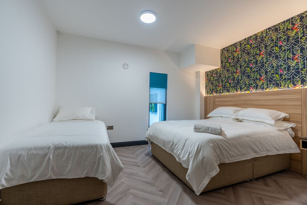 A hotel room with two single beds, a wooden headboard, a patterned wall, and a small window.