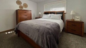 Un dormitorio con cama, mesita de noche, cómoda y ventana con persianas.