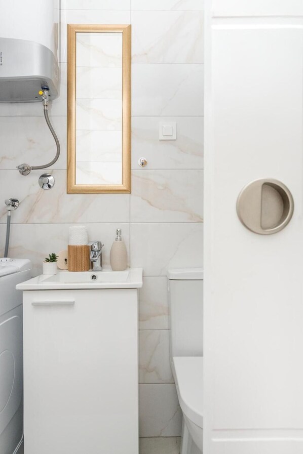 Un baño con lavamanos blanco, un espejo, inodoro y ducha.