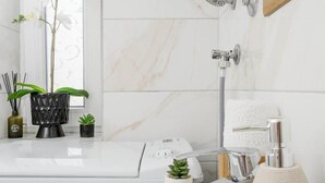 Un bagno moderno con vasca, doccia e WC. Sul mobile del lavabo ci sono piante decorative e un vaso.