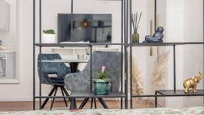 Un soggiorno moderno con un divano grigio, un tavolo da pranzo e una TV. Sono presenti elementi decorativi come una statua e una pianta su mensole.