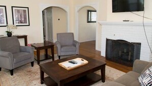 A living room with a fireplace, two armchairs, a coffee table, and a television mounted on the wall. - Yakima Vacation Rentals- Spacious Bungalow
 (Yakima)