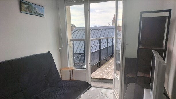 A room with a bed, a desk with a laptop, a TV, and a window overlooking a rooftop. - Terrace apartment in Merlimont (Merlimont)