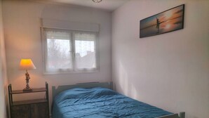 A bedroom with a bed, a bedside table with a lamp, a window with curtains, and a painting on the wall. - Terrace apartment in Merlimont (Merlimont)