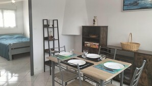 A compact room with a bed, a dining table set for two, a small cabinet, and a wall-mounted shelf. - Terrace apartment in Merlimont (Merlimont)