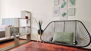A modern living room with a sofa, a wooden coffee table, a black wire chair, a wooden bookshelf, and wall art. - Large Apartment Villa Urquiza (Buenos Aires)