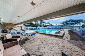 An outdoor pool area with lounge chairs, a covered seating area, and a view of the surrounding buildings.