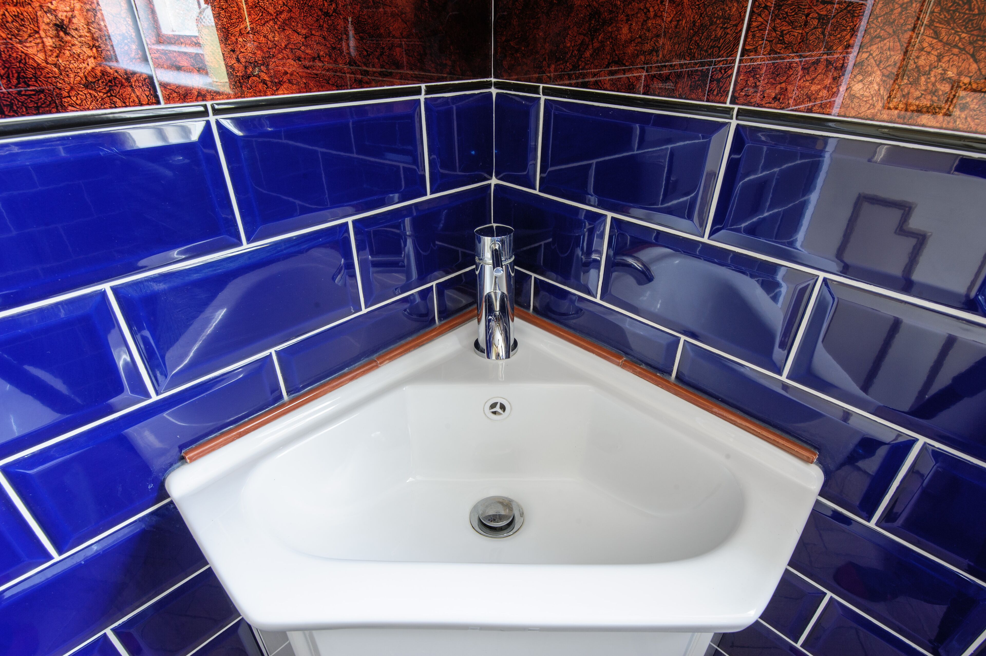 Une salle de bain avec un lavabo blanc, des carreaux bleus et un plan de travail en bois.