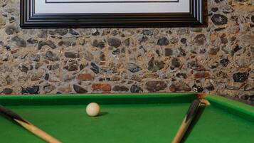 Une photographie encadrée représentant une personne se relaxant sur un canapé, une table de billard avec des billes, et un mur en pierre.