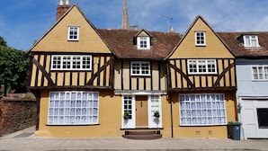 Una casa tradicional de estilo Tudor con fachada simétrica, dos chimeneas y una puerta central con un pequeño porche.