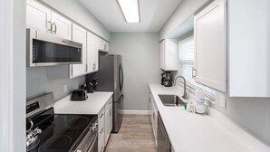 A compact kitchen with white cabinetry, a microwave, a refrigerator, a stove, and a sink. - Aloha Kai Villa 10 - Premium Siesta Key Beach (Siesta Key)
