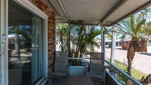 A covered balcony with two wicker chairs and a small table, a glass door, and a view of palm trees and a residential area. - Aloha Kai Villa 10 - Premium Siesta Key Beach (Siesta Key)