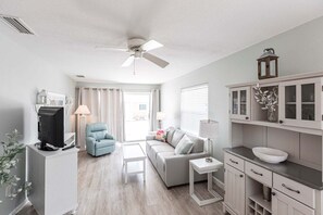 A modern living room with a grey sofa, a blue armchair, a white coffee table, and a television on a white stand.