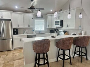 A modern kitchen with white cabinets, a stainless steel refrigerator, a built-in oven, and a central island with bar stools.
