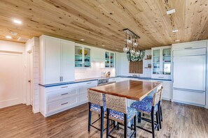 A kitchen with white cabinets, a wooden ceiling, and a central island with chairs.