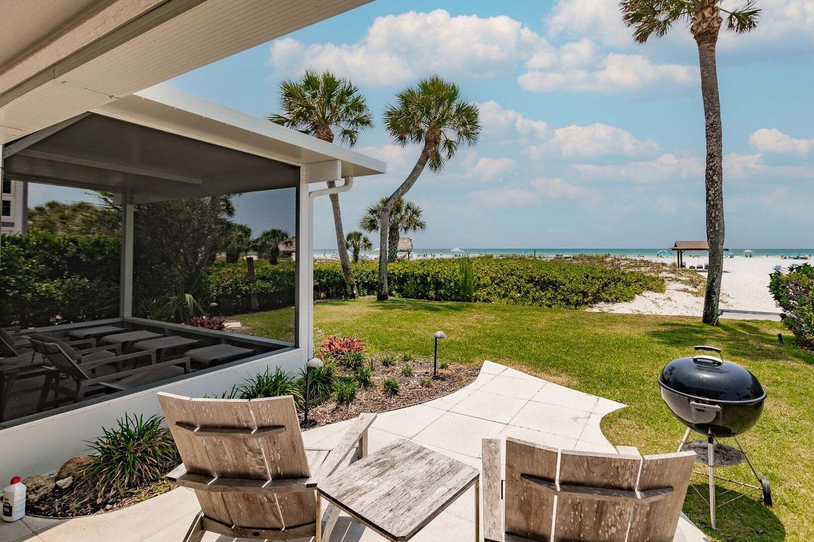 An outdoor patio with a view of the beach, a grill, and seating.