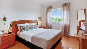 A bedroom with a bed, a nightstand, a dresser, a window with curtains, and a view of greenery outside. - Golden 1 BDR Flat W/ Balcony & Pool by LovelyStay (Cabanas)
