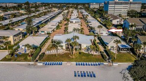 A resort with multiple buildings, a beach area with sun loungers, and a parking lot.