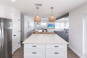 A modern kitchen with a large island, white cabinetry, and two hanging wicker pendant lights.