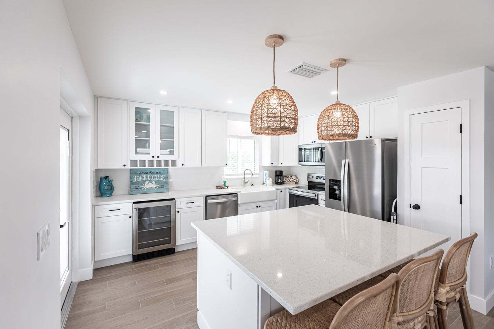 A modern kitchen with white cabinetry, a large island, stainless steel appliances, and wicker pendant lights.