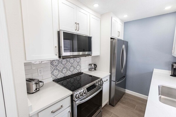 A modern kitchen with white cabinets, a stainless steel refrigerator, a built-in oven, and a microwave.