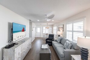 A modern living room with a television, a grey sofa, a black chair, and a dining area with a table and chairs.
