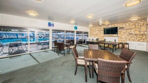 An indoor dining area with a view of an outdoor pool, stone wall, and ceiling fans.