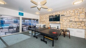 A conference room with a large table, chairs, a ceiling fan, a stone wall, a TV, and a view of an outdoor pool.