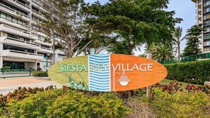 A sign for Siesta Key Village with a modern building in the background.