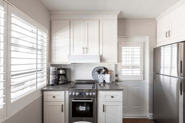 A kitchen with white cabinets, a stainless steel refrigerator, a built-in oven, and a coffee maker.