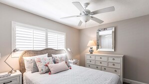 A bedroom with a bed, bedside tables, a dresser, a ceiling fan, and a window with blinds.