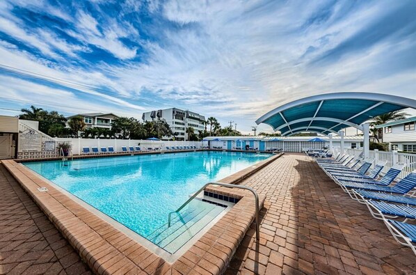 A swimming pool with lounge chairs, a covered area, and a clear sky.
