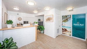A reception area with a wooden counter, potted plants, a clock, and a door leading to a room with a beach view poster. - Aloha Kai Villa 32 - Premium Siesta Key Beach (Siesta Key)