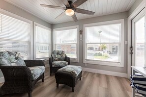 A sunroom with wicker furniture, large windows, and a ceiling fan.