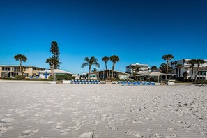 Een strand met ligbedden en palmbomen, met hotelgebouwen op de achtergrond.