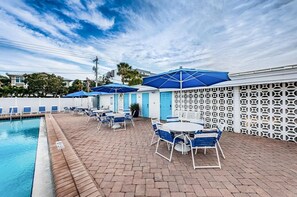Zona junto a la piscina con sillones de descanso y sombrillas, una piscina y una cerca decorativa.