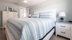 Un dormitorio con cama, mesitas de noche, ventilador de techo y una puerta.
