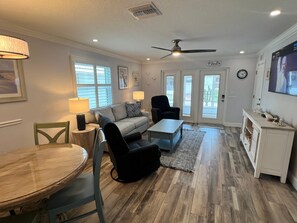 A living room with a sofa, chairs, a coffee table, a TV, and a dining area with a table and chairs.