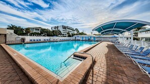A swimming pool with a sunshade, lounge chairs, and a brick deck.