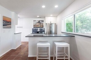 A modern kitchen with a bar area, stainless steel appliances, and a large window.