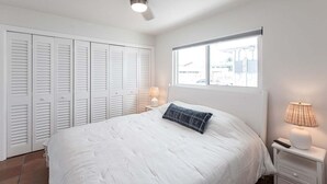 A bedroom with a bed, a ceiling fan, a window, and a nightstand with a lamp.
