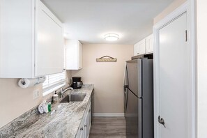 A compact kitchen with white cabinets, a stainless steel refrigerator, a coffee maker, and a wall-mounted sign.